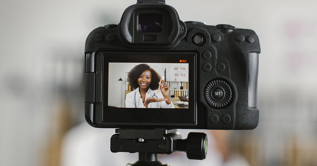 woman with dark curly hair in font of a camera recording a video