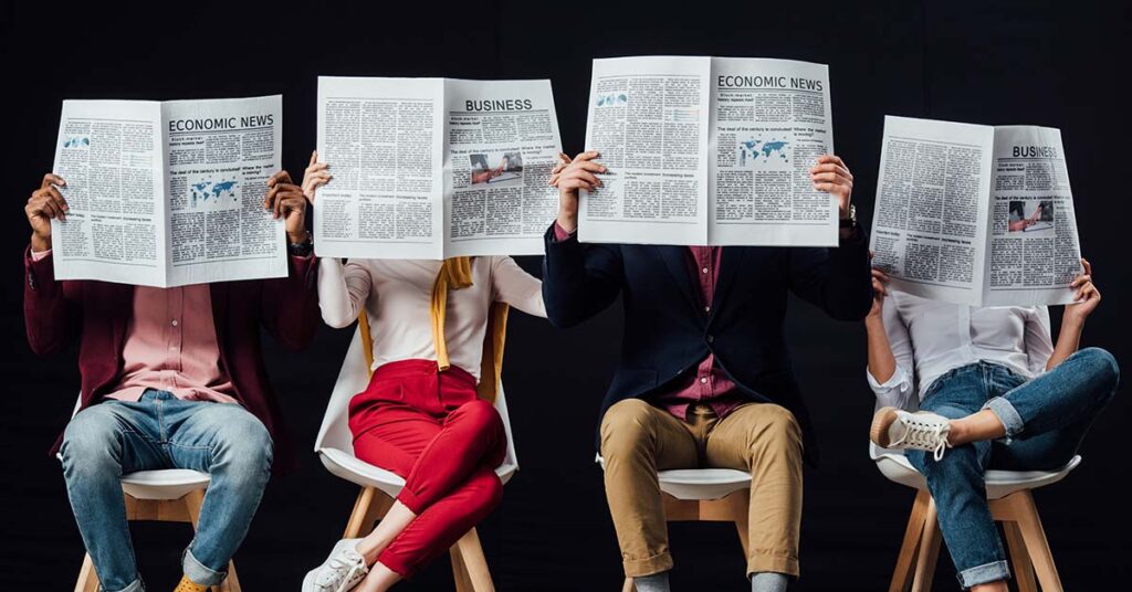 four people sat on chairs next to each other reading newspapers