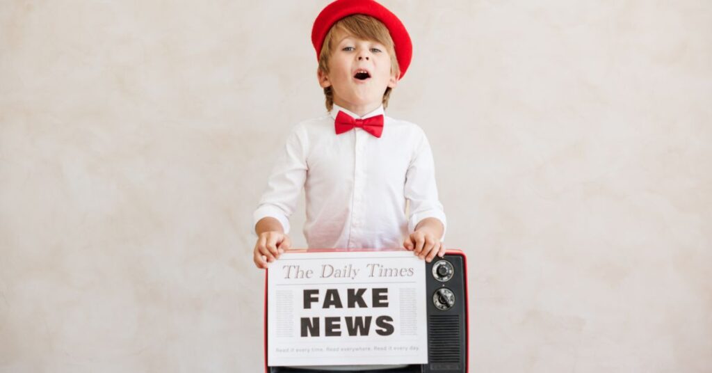 Small young boy in a red hat holding a sign which says 'Fake News'