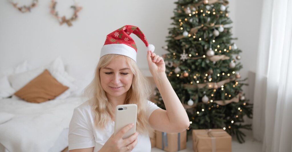 Woman on the phone wearing a Christmas hat with a Christmas tree in the background