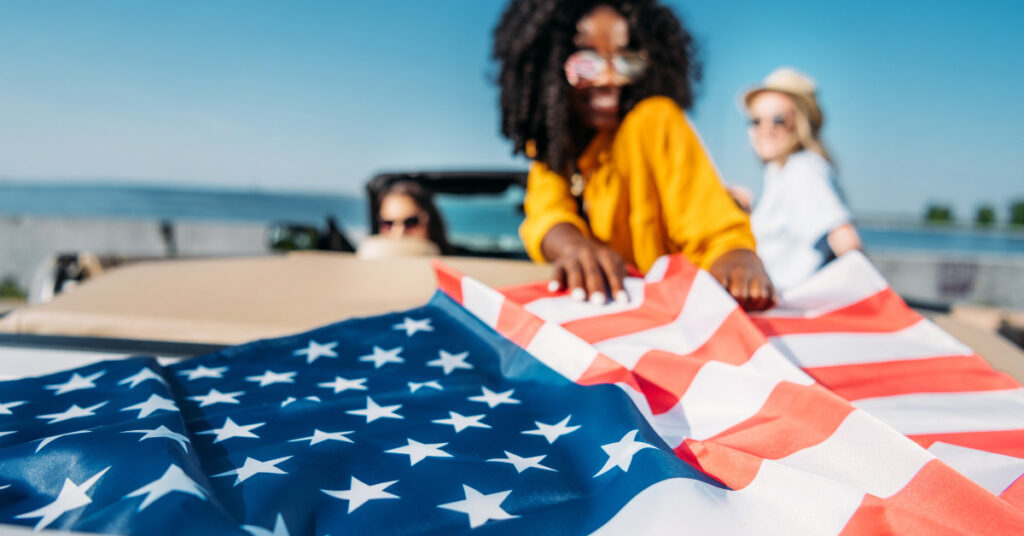 girl, black hair, curly hair, holding USA flad on the beach